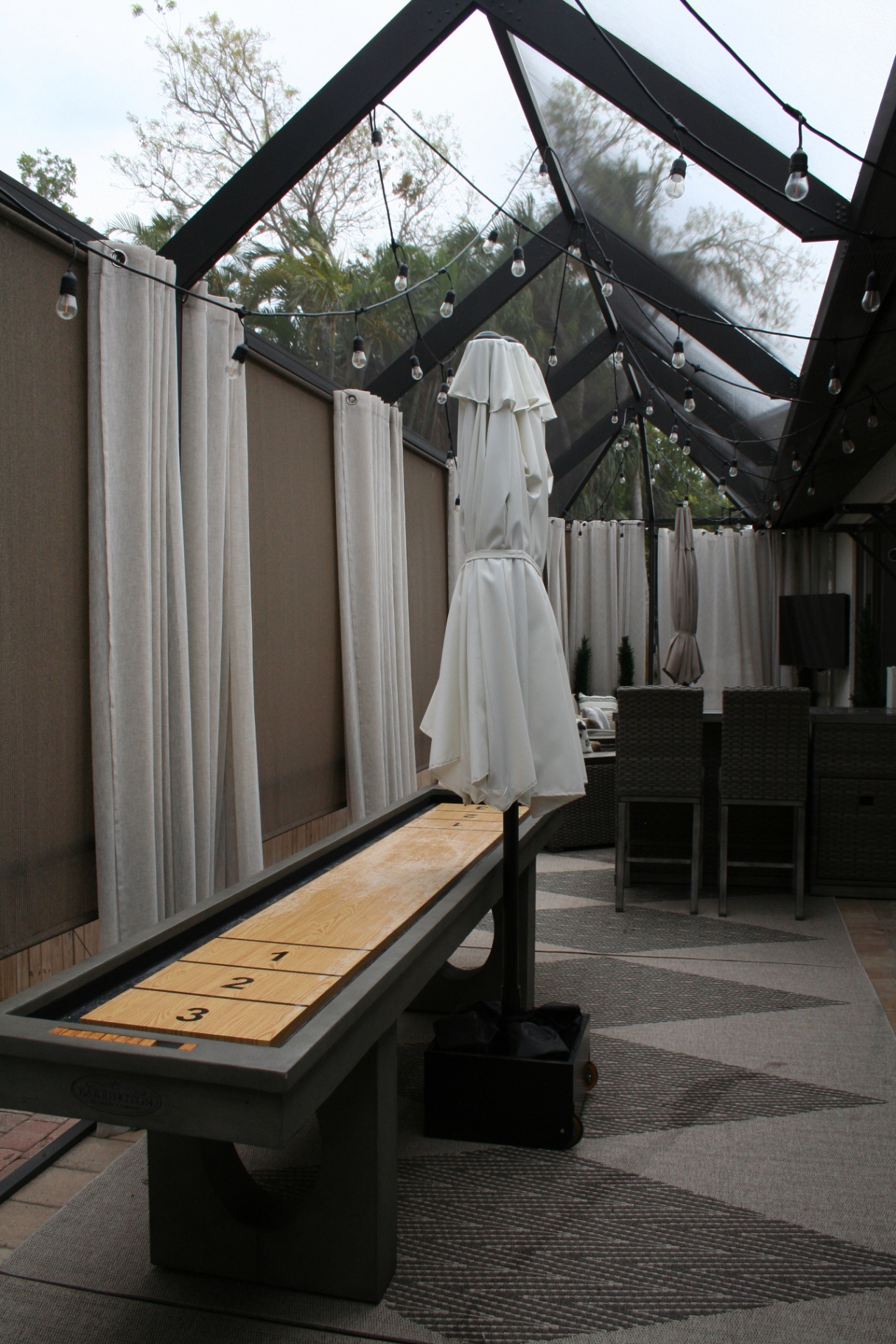 Shuffleboard table under peaked lanai roof with string lights and palm view